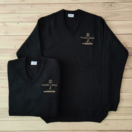Black V-neck knit sweaters with gold embroidered housekeeping logo, two sizes laid flat, custom made for Elgin Hall by RestroCart, New Delhi