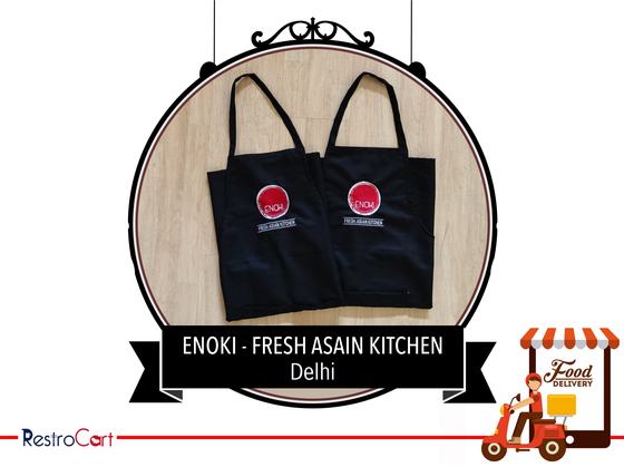 Pair of black bib aprons with round red logo printed at chest height, straps spread out, custom made for Enoki Kitchen by RestroCart, New Delhi