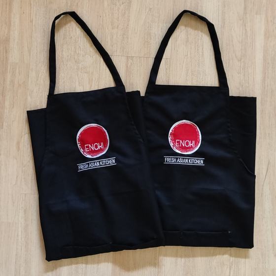 Two black bib aprons with round red brushstroke logo and white tagline, custom made for Enoki Kitchen by RestroCart, New Delhi