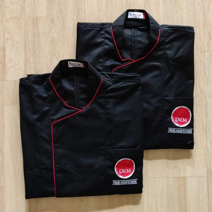 Black wrap-front chef coats with red piping along the crossover and a red round logo, custom chef uniforms made for Enoki Kitchen by RestroCart