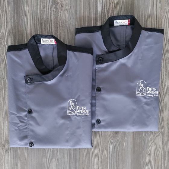Two grey chef coats with black collar and shoulder yoke and white bakery logo, folded, custom made for Fifth Avenue Bakery by RestroCart, New Delhi