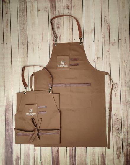 Golden brown canvas apron pair with leatherette pocket patch and small printed logo, custom made by RestroCart, New Delhi