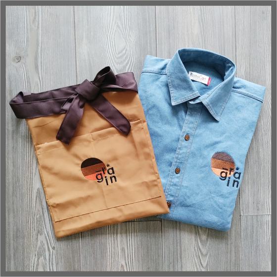 Tan waist apron with brown ties and light blue denim shirt, both with round colour-block logo, custom made for Grain by RestroCart, New Delhi