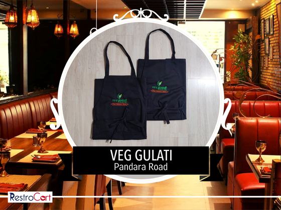 Two black bib aprons with green and red embroidered logo and waist ties, laid flat, custom made for Gulati by RestroCart, New Delhi
