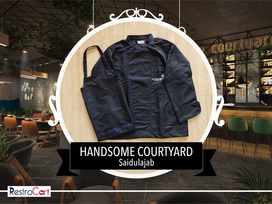 Navy chef coat with blue piping and embroidered logo beside a navy bib apron, laid flat, custom made for Handsome Courtyard by RestroCart, New Delhi
