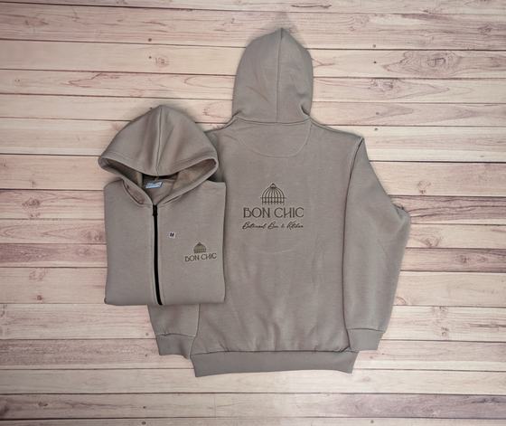 Beige zip hoodies with dark embroidered pavilion logo on back and chest, one folded, custom made by RestroCart, New Delhi
