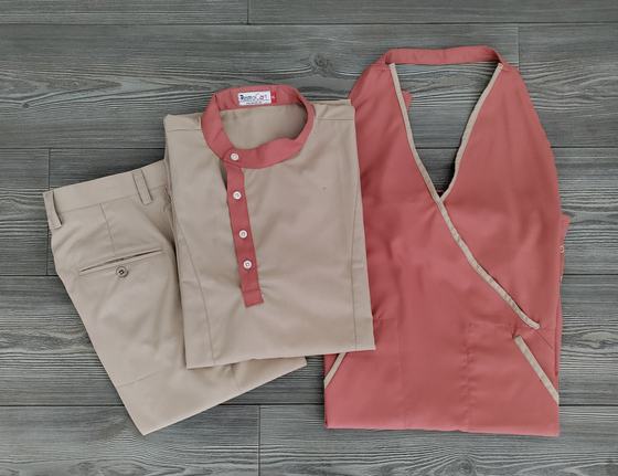 Beige tunic with coral collar and placket, beige trousers and coral cross-over apron with beige piping, custom made by RestroCart, New Delhi