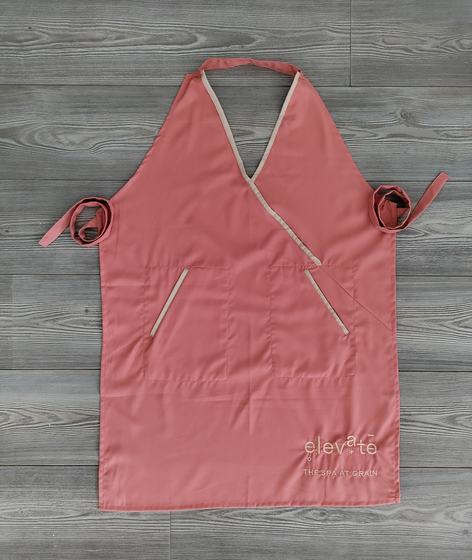 Coral cross-over bib apron with beige piping, side ties and small printed logo, laid flat, custom made by RestroCart, New Delhi
