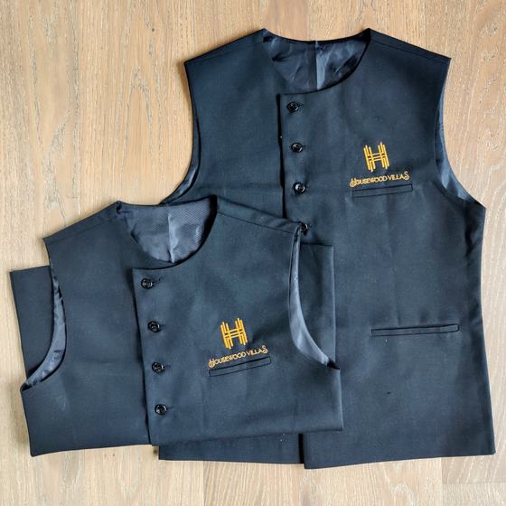 Two navy sleeveless Nehru waistcoats with gold embroidered logo and button front, laid flat, custom made for Housewood Villas by RestroCart, New Delhi