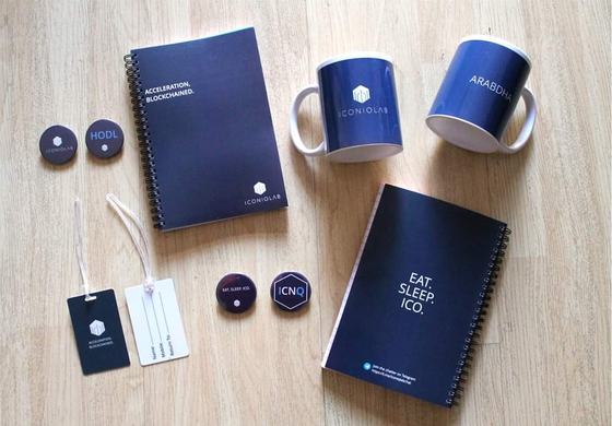 Branded corporate gift kit for IconiqLab laid out flat: navy notebooks, printed mugs, round badges and luggage tags, made by RestroCart
