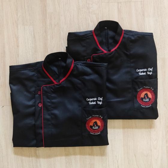 Two folded black chef coats with red piping, embroidered chef name and round logo on pocket, custom made for Ikura by RestroCart, New Delhi