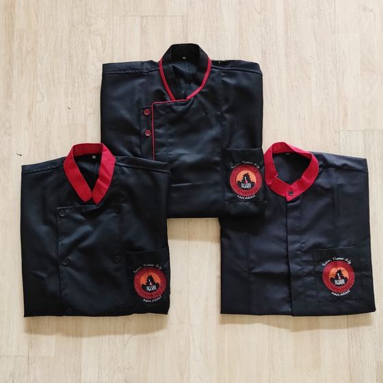 Three folded black chef coats with red collars and round printed logo on sleeve pocket, custom made for Ikura by RestroCart, New Delhi