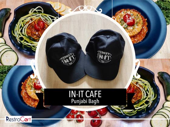 Two black baseball caps with white round printed logo, set side by side on wood, custom made for In It Cafe by RestroCart, New Delhi