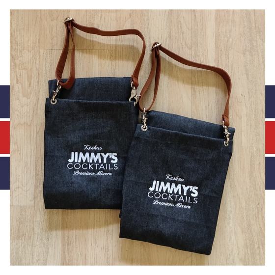 Two dark denim bib aprons with brown leather straps and white printed logo, laid flat, custom made for Jimmy's Cocktails by RestroCart, New Delhi