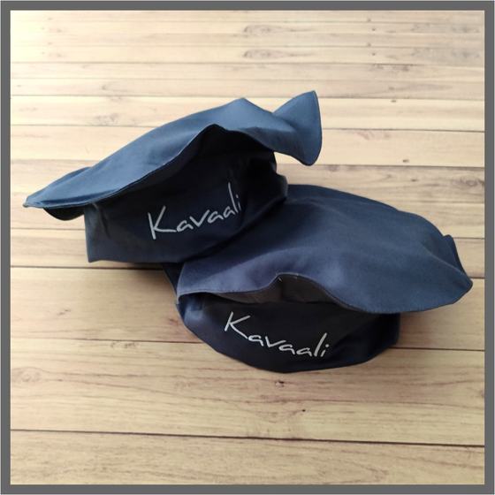 Two charcoal grey chef caps with white embroidered script logo on band, close-up on wooden floor, custom made for Kavaali by RestroCart, New Delhi