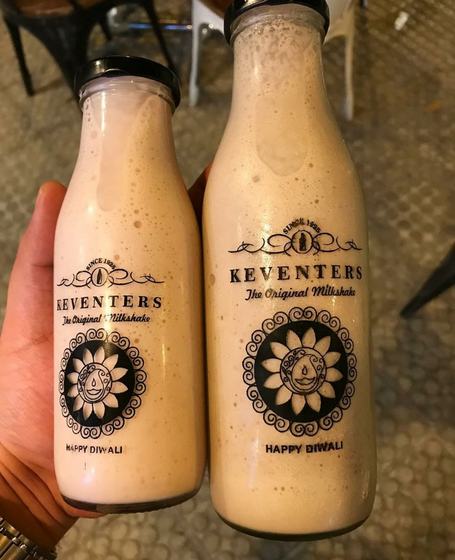 Two glass milkshake bottles with black screen printed logo and floral emblem, held in hand, custom made for Keventers by RestroCart, New Delhi