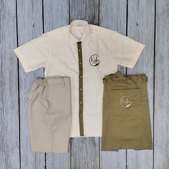 Cream half sleeve shirt with olive placket, beige trousers and olive apron with round logo, custom made for Kiki Bar by RestroCart, New Delhi