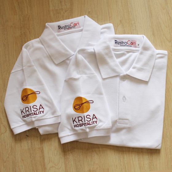 Two white polo T-shirts with large orange embroidered logo on sleeve, folded, custom made for Krisa Hospitality by RestroCart, New Delhi