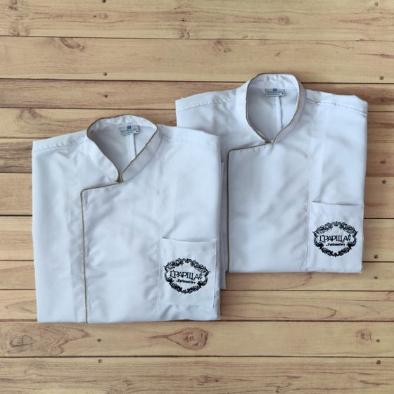 Two white chef coats with gold piping and black embroidered wreath logo on pocket, folded, custom made for L'Papillae by RestroCart, New Delhi