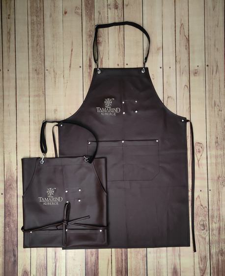 Dark brown leatherette bib aprons in two sizes with rivets, pockets and embossed gold logo, custom made by RestroCart, New Delhi