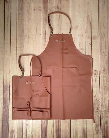 Tan leatherette bib aprons in two sizes with leather neck strap, rivets and embossed logo, custom made by RestroCart, New Delhi