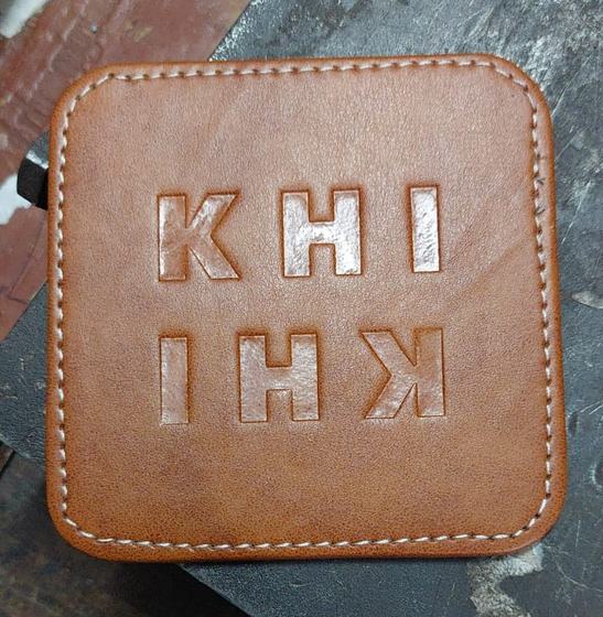 Close-up of a tan square leatherette coaster with stitched edge and embossed mirrored letters, custom made by RestroCart, New Delhi