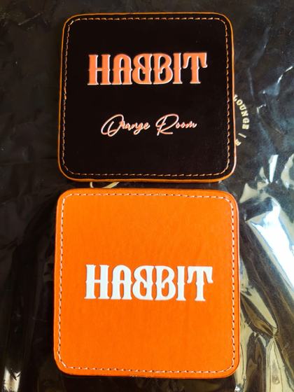 Square leatherette coasters in black and orange with stitched edges and printed bold logo, custom made by RestroCart, New Delhi