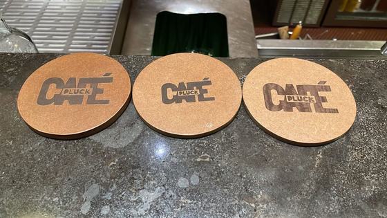 Three round brown coasters with laser-engraved block logo lined up on a stone bar counter, custom made by RestroCart, New Delhi