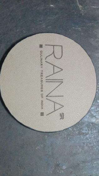 Round grey leatherette coaster with debossed vertical wordmark and tagline, on a slate surface, custom made by RestroCart, New Delhi