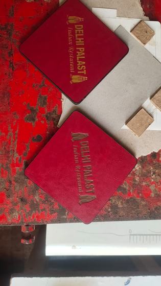 Square red leatherette coasters with gold foil printed logo beside cork backing squares, custom made by RestroCart, New Delhi