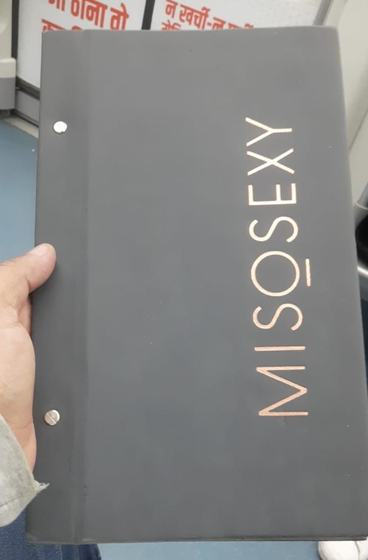 Grey leatherette menu cover with screw binding and vertical rose gold printed wordmark, held in hand, custom made by RestroCart, New Delhi