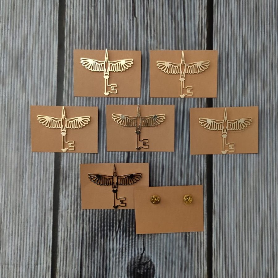 Gold metal lapel pins in a winged key design on kraft backing cards, custom made for Lord Elgin by RestroCart