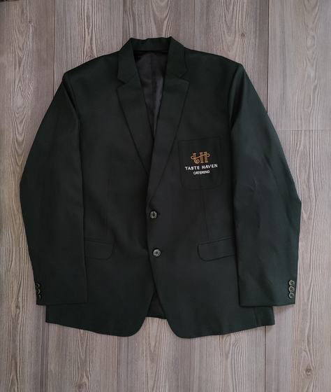 Black manager blazer with gold embroidered crest logo on breast pocket, laid flat, custom made by RestroCart, New Delhi