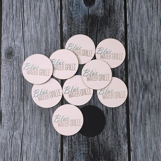 Round blush pink MDF coasters with teal printed grille wordmark, arranged in a cluster, custom made by RestroCart, New Delhi