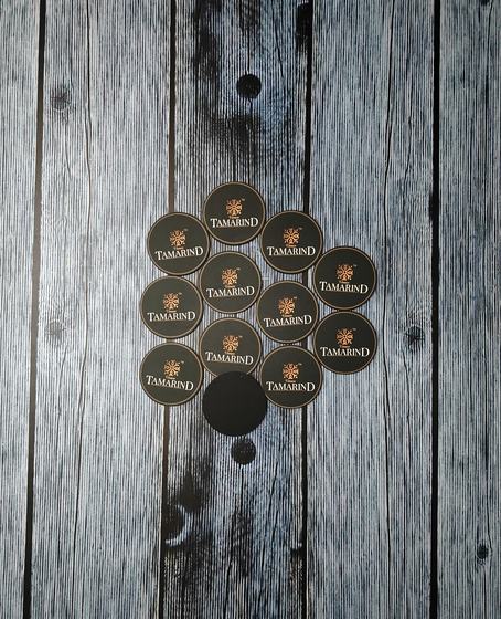 Small round black MDF coasters with gold printed emblem and wordmark in a tight cluster, custom made by RestroCart, New Delhi