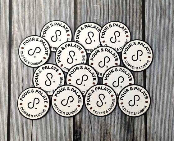 Set of round white MDF coasters with black printed circular coffee and cuisine logo, on grey wood, custom made by RestroCart, New Delhi