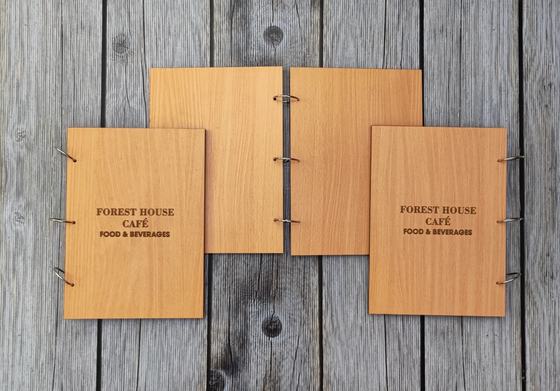 Four light wood MDF menu covers with engraved cafe name and metal binder rings, on grey wood, custom made by RestroCart, New Delhi