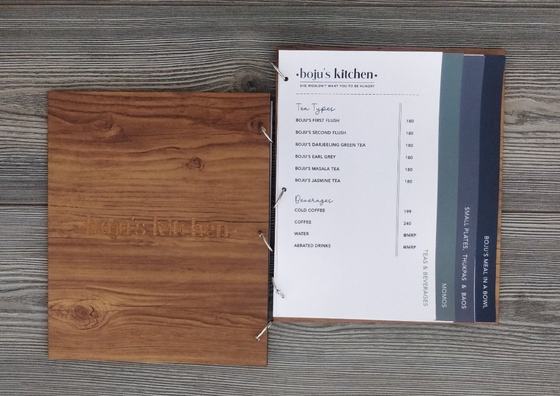 Wood grain MDF menu cover with engraved logo beside ring-bound printed menu pages with tabs, custom made by RestroCart, New Delhi