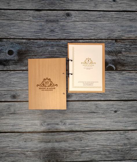 Light wood MDF ring-bound menu cover with laser-engraved crest beside a cream printed inner menu page, custom made by RestroCart, New Delhi