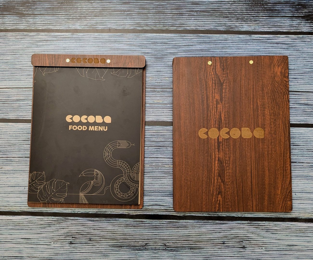 Two walnut-finish MDF menu boards, one with a screw-post header strip holding a black printed food menu insert and one with a gold logo on the woodgrain cover, made by RestroCart