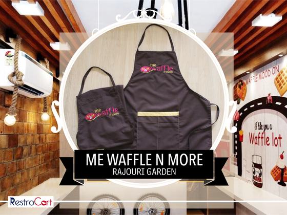 Two dark grey bib aprons with pink and white logo and gold waist stripe, laid flat, custom made for Me Waffle N More by RestroCart, New Delhi