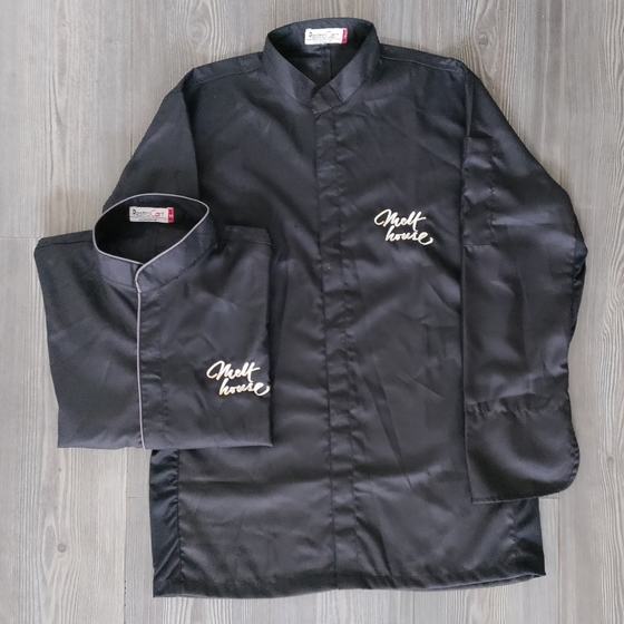 Two black long sleeve chef coats with grey piping and white embroidered script logo, laid flat, custom made for Melt House by RestroCart, New Delhi