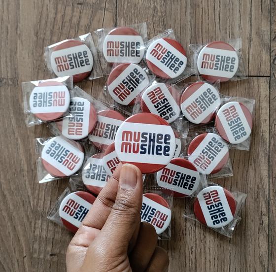 A pile of red and white printed round button badges held up in a hand on a wooden table, custom badges made by RestroCart