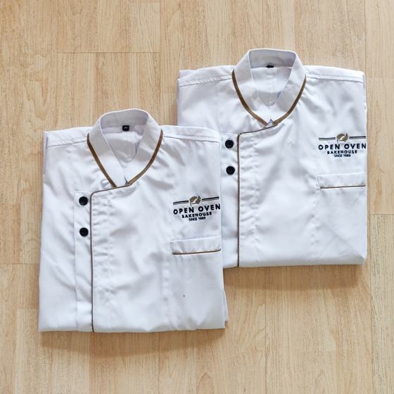Two white chef coats with brown crossover piping, black buttons and embroidered logo, custom made for Open Oven Bakehouse by RestroCart, New Delhi