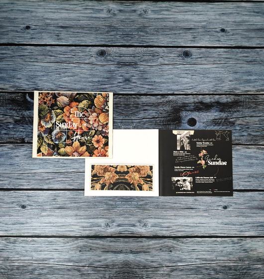 Square printed paper menus with a floral tapestry cover and a black dessert page inside, on a grey wooden surface, printed by RestroCart