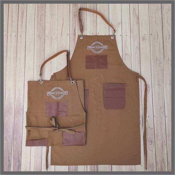 Two brown canvas bib aprons with leatherette pockets and round logo, adult and small size, custom made for Peggy Ice Creams by RestroCart, New Delhi