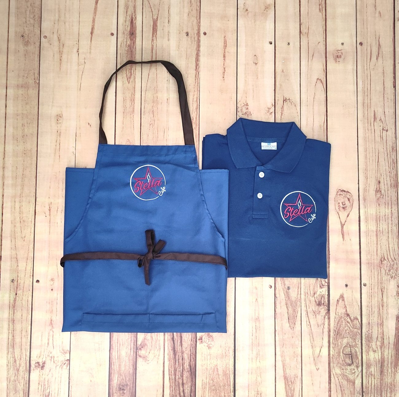 Custom navy polo t-shirt with a royal blue bib apron, both with embroidered branding, a service uniform set made by RestroCart, New Delhi