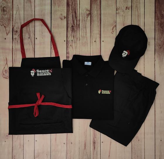Black polo t-shirt, black cap, black trousers and black bib apron with red straps, all printed with logo, custom made by RestroCart, New Delhi