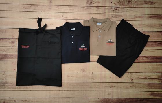 Navy and beige polo t-shirts with black waist apron and black trousers, laid in a row, custom made by RestroCart, New Delhi
