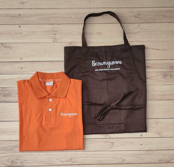 Orange polo t-shirt with white script logo and brown bib apron with white printed script, custom made by RestroCart, New Delhi